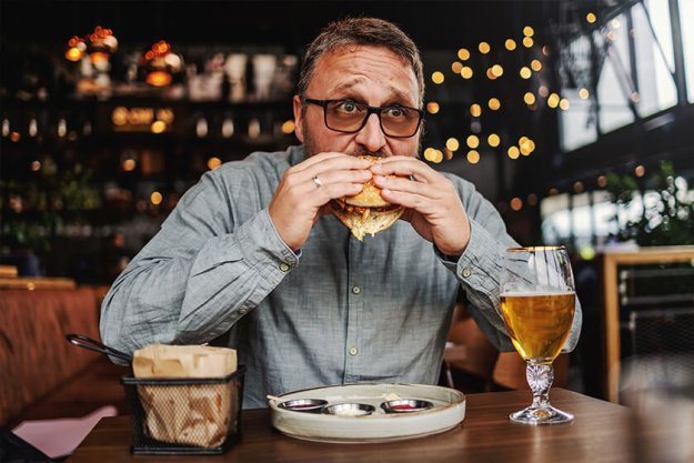 Middle aged bearded hungry man sitting in restaurant and eating delicious burger Middle aged bearded hungry man sitting in restaurant and eating delicious burger