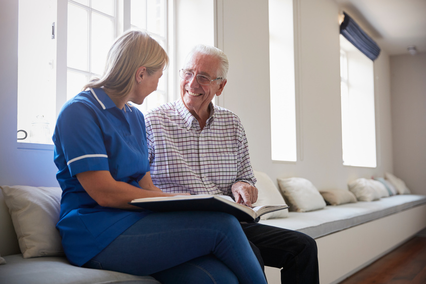 Senior man sitting looking at photo album with care nurse Alzheimer's In Seniors: 4 Ways Memory Care Facility In Lower Greenville, TX Can Help Slow Down The Progression