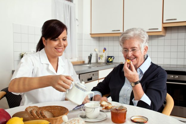 nurse helps elderly woman at breakfast 5 Signs Your Aging Parent Needs 24-Hour Care In A Highland Park, TX Senior Home