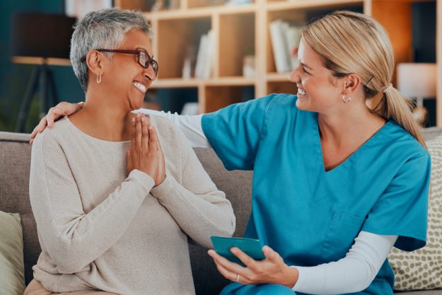 Senior care, caregiver and patient together on a couch talking about healthcare of hospice service leaflet, brochure or booklet. Elderly woman and nurse at home for care with gratitude for help Learn Who's Behind The Success Of Your Parent's Care In Memory Care Units In Fort Worth, TX