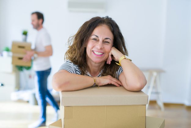 Middle age senior couple moving to a new house, woman smiling ha Why Should Seniors Downsize To Retirement Apartments In North Dallas, TX?