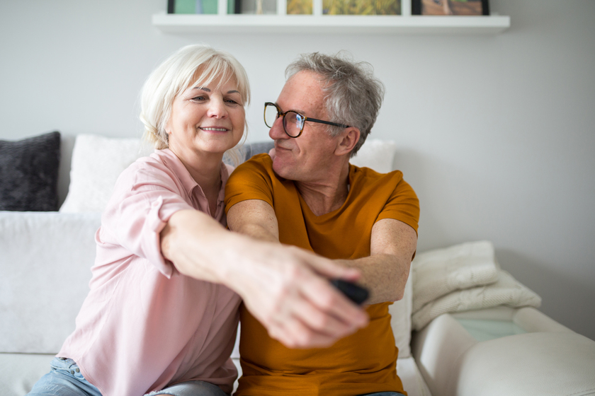 Happy senior couple holding tv remote together Aging In Place With Purpose: Exploring Intentional Retirement Communities In Park Cities, TX