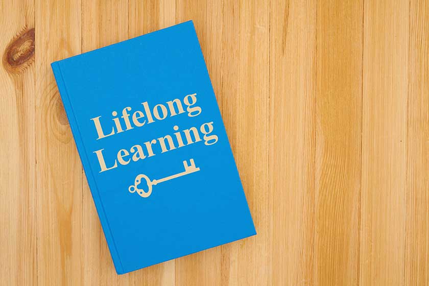 Lifelong learning message with a skeleton key icon written on a book on a wood desk