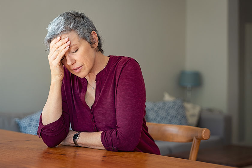 Senior woman suffering from headache while sitting in table Senior woman suffering from headache while sitting in table