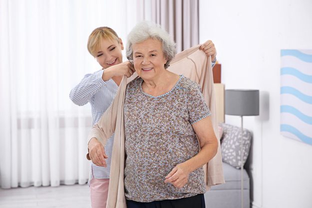 Caregiver helping senior woman to put on cardigan Caregiver helping senior woman to put on cardigan