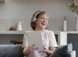 Happy elderly woman in headphones using digital touchpad gadget.