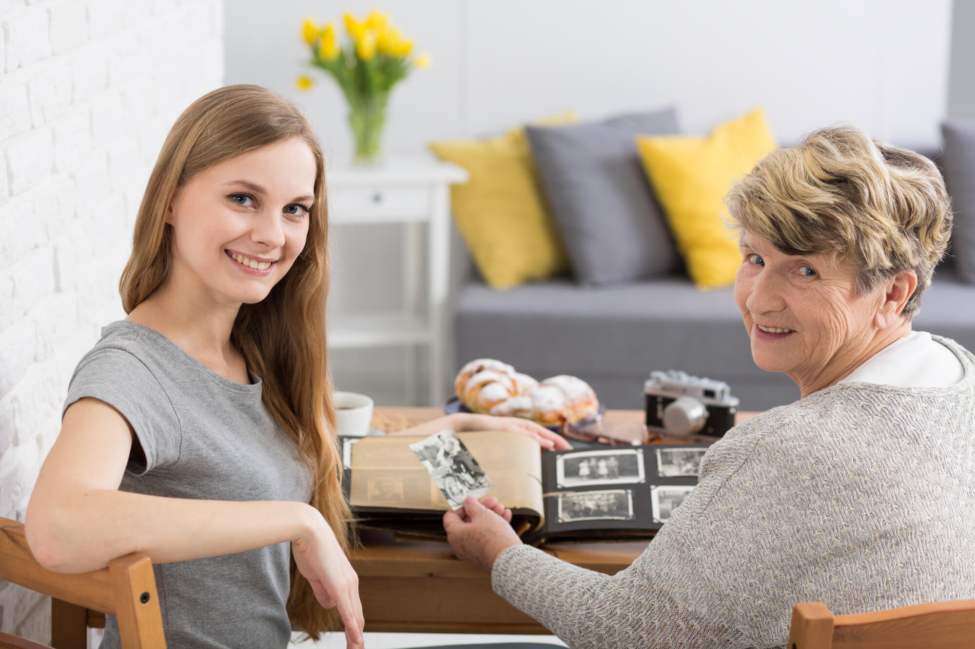 Granddaughter,And,Grandmother,Smiling,At,A,Camera,,Watching,Old,Photographs