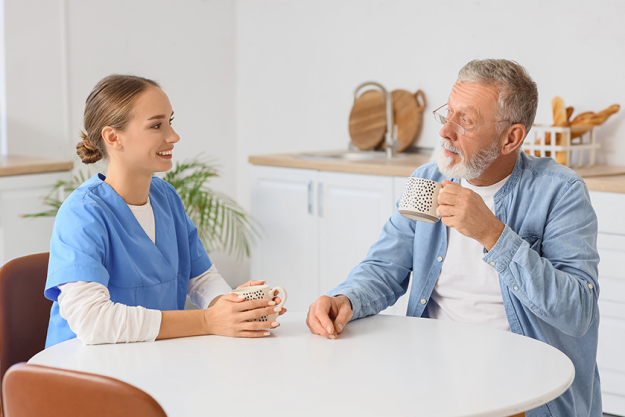 Senior man with nurse drinking tea in kitchen