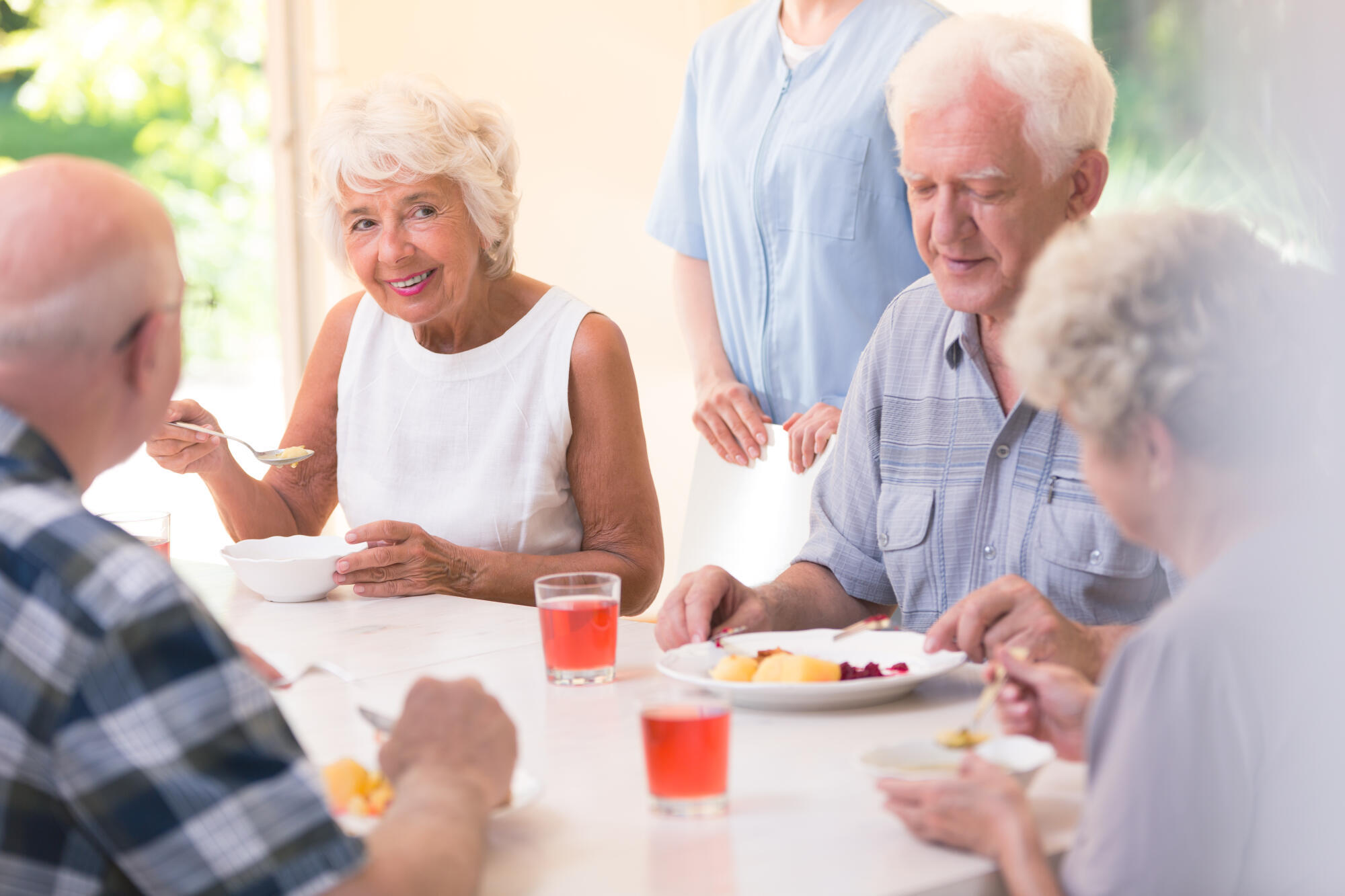 Smiling,Senior,Woman,Eating,Soup,With,Friends,While,Sitting,At