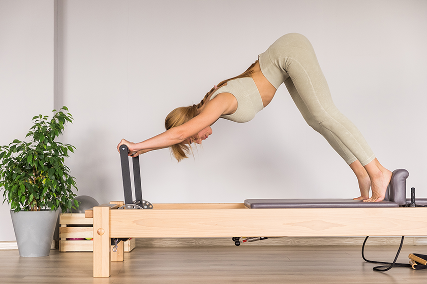 woman-training-pilates-reformer-bed-reformer-pilates-studio Woman training pilates on the reformer bed.
