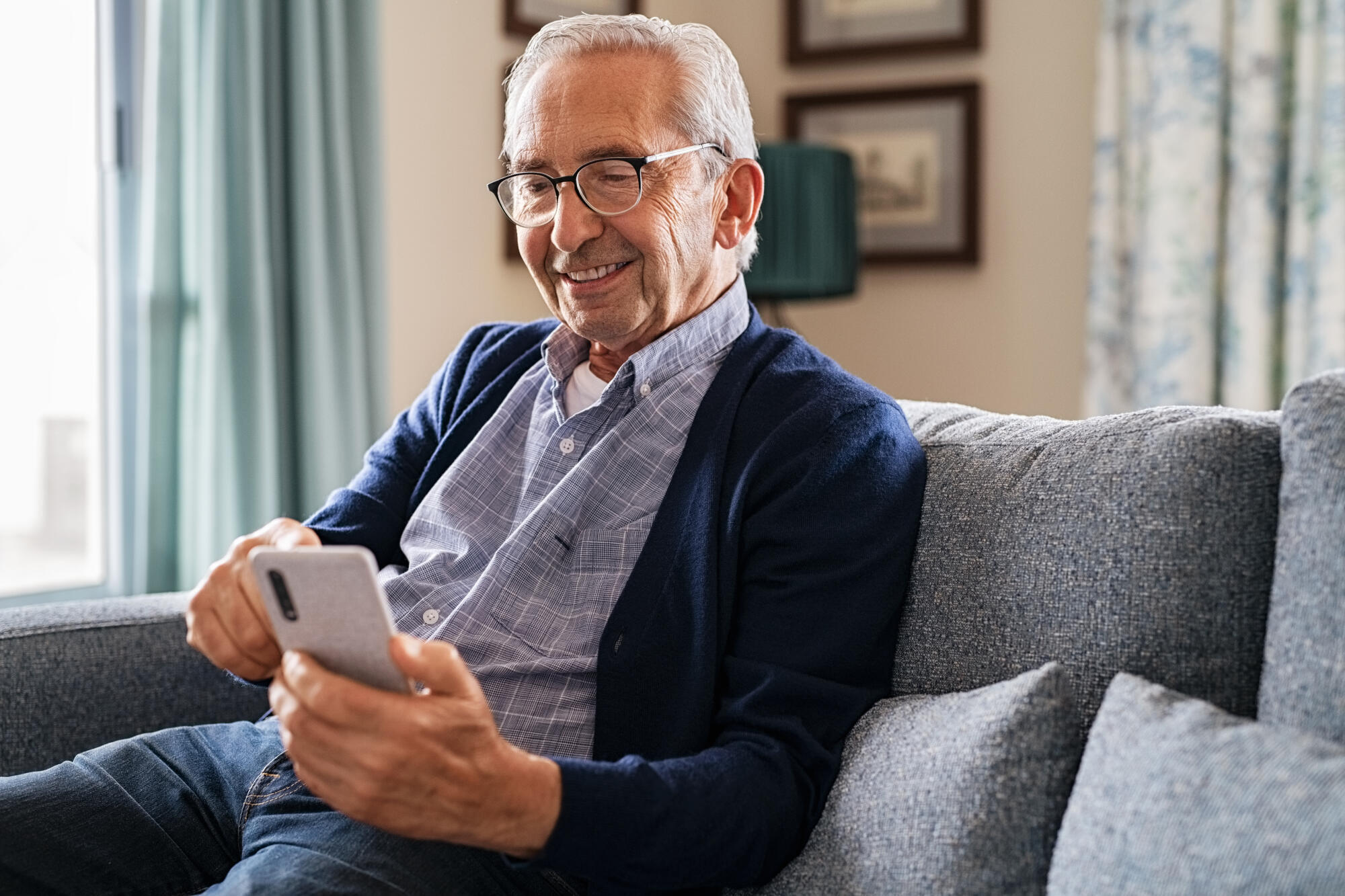 Smiling,Old,Man,Using,Smartphone,While,Sitting,On,Couch.,Happy